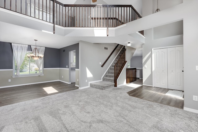 unfurnished living room featuring carpet flooring, a high ceiling, a chandelier, stairway, and baseboards