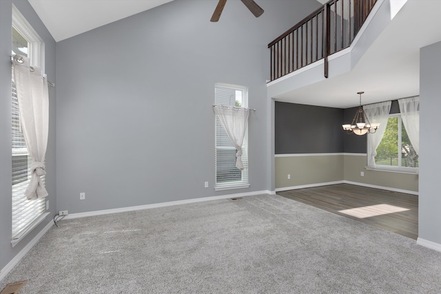 carpeted empty room featuring a chandelier, ceiling fan, high vaulted ceiling, and baseboards
