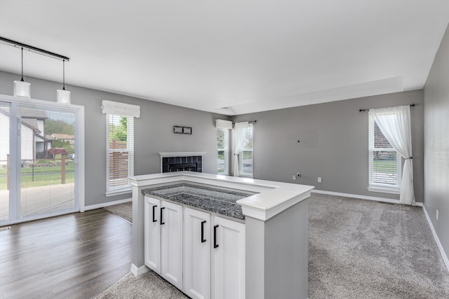 kitchen featuring open floor plan, baseboards, a tiled fireplace, white cabinetry, and hanging light fixtures