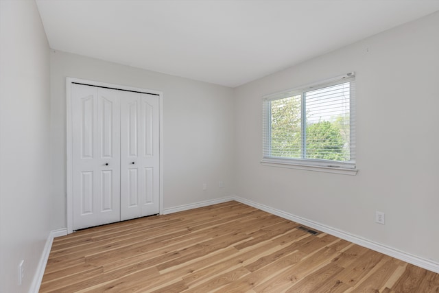 unfurnished bedroom featuring light wood-style floors, baseboards, and a closet