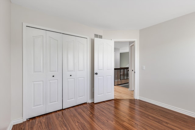unfurnished bedroom featuring wood finished floors, baseboards, and a closet
