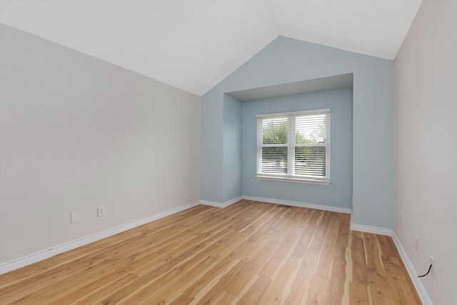 spare room featuring light wood-style floors, vaulted ceiling, and baseboards