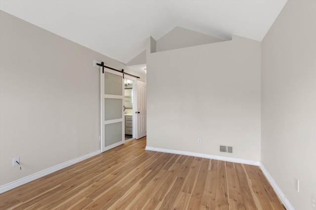 spare room with a barn door, vaulted ceiling, light wood-style flooring, and baseboards