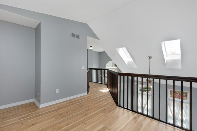 additional living space with a skylight, wood finished floors, vaulted ceiling, and baseboards