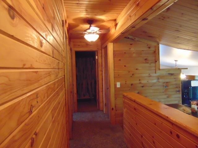 corridor featuring wooden walls, wood ceiling, and carpet flooring