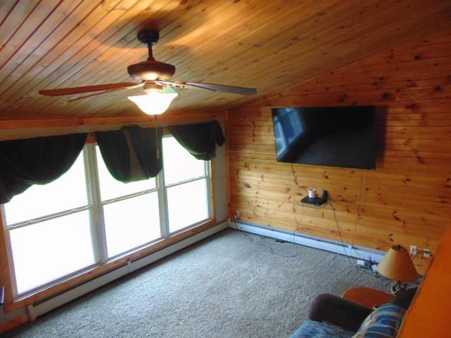 unfurnished living room featuring carpet floors, wood ceiling, a ceiling fan, wood walls, and lofted ceiling