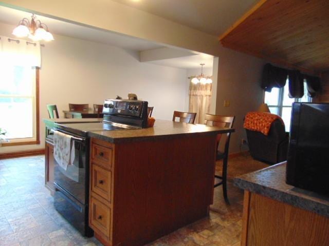 kitchen featuring black / electric stove, a chandelier, a breakfast bar, brown cabinets, and dark countertops
