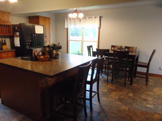 kitchen with black fridge with ice dispenser, dark stone finish flooring, a breakfast bar area, a chandelier, and a kitchen island