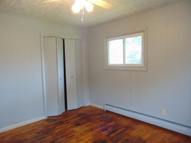 unfurnished bedroom with a baseboard radiator, wood finished floors, a closet, and baseboards