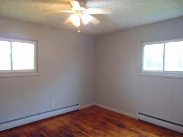 spare room featuring baseboard heating, wood finished floors, a ceiling fan, and baseboards