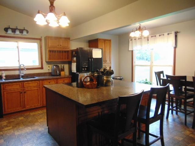 kitchen featuring black refrigerator with ice dispenser, a chandelier, a sink, a kitchen breakfast bar, and a center island