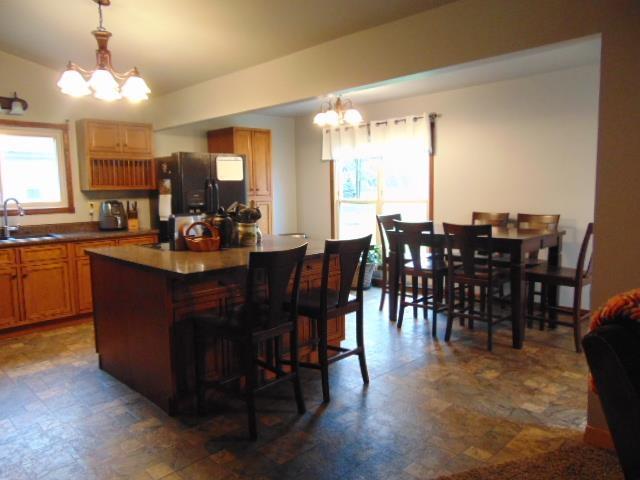 kitchen featuring a chandelier, black refrigerator with ice dispenser, a sink, a center island, and a breakfast bar