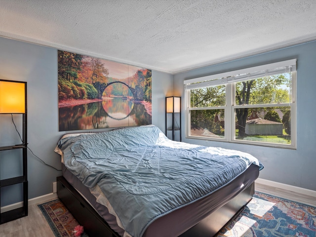 bedroom with a textured ceiling, wood finished floors, baseboards, and a water view