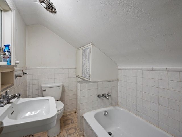 bathroom with tile walls, a bath, a sink, lofted ceiling, and toilet