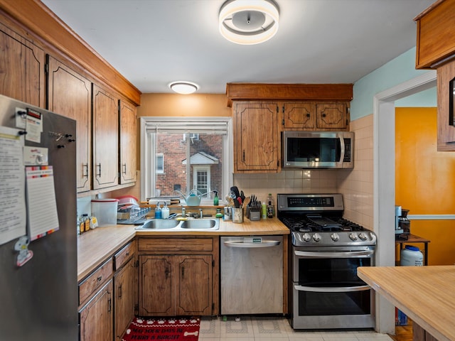kitchen with appliances with stainless steel finishes, light countertops, backsplash, a sink, and brown cabinets