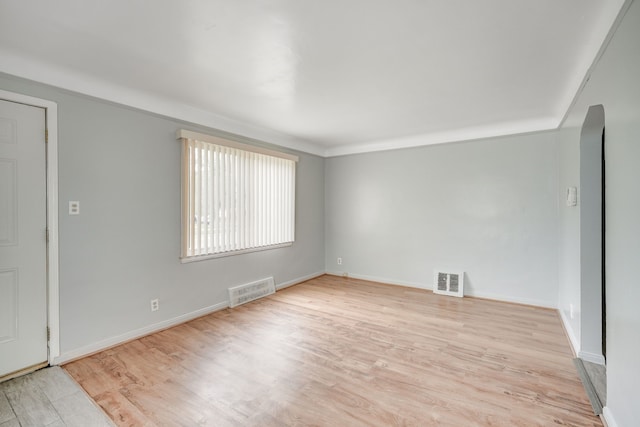 empty room featuring light wood finished floors, baseboards, and arched walkways