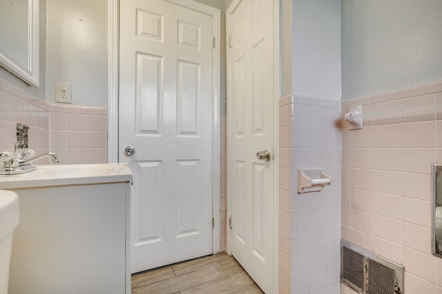 bathroom with tile walls, wood finished floors, vanity, and a wainscoted wall