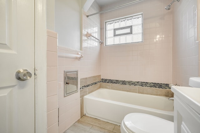 bathroom featuring toilet, vanity, shower / bath combination, and tile walls
