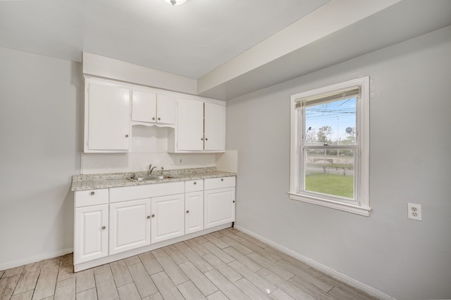 kitchen with a sink, baseboards, white cabinets, and light wood finished floors