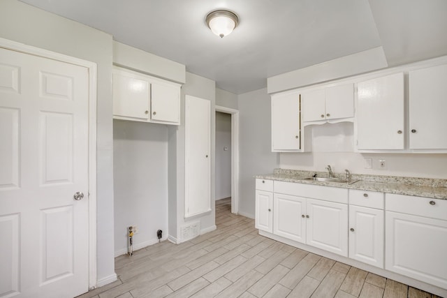 kitchen with baseboards, white cabinets, light wood finished floors, and a sink