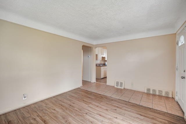 unfurnished room with arched walkways, light wood-type flooring, a textured ceiling, and baseboards