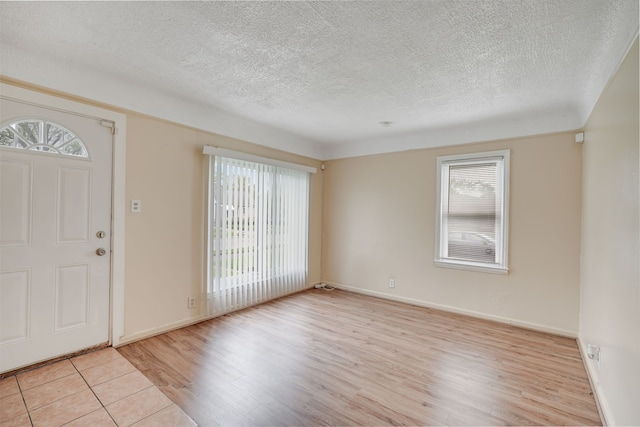 foyer entrance featuring plenty of natural light, light wood-style flooring, a textured ceiling, and baseboards
