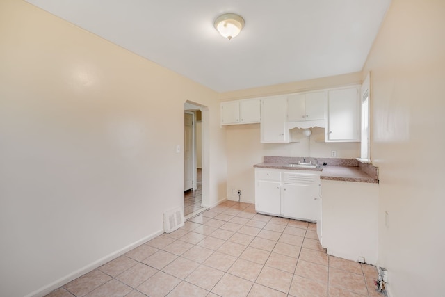 kitchen with arched walkways, white cabinetry, light tile patterned flooring, a sink, and baseboards
