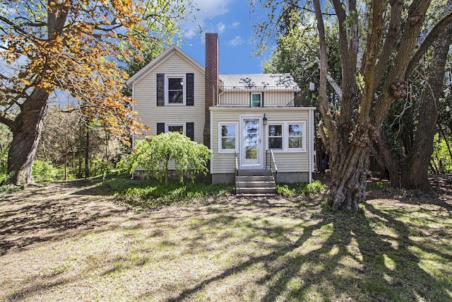 traditional home with entry steps, a chimney, and a front lawn