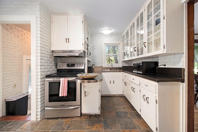 kitchen featuring stainless steel electric stove, under cabinet range hood, a sink, stone finish floors, and dark countertops