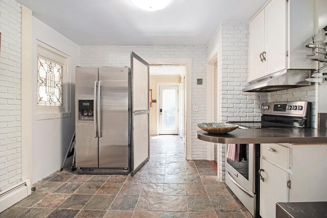 kitchen featuring appliances with stainless steel finishes, a baseboard heating unit, stone tile floors, dark countertops, and white cabinetry