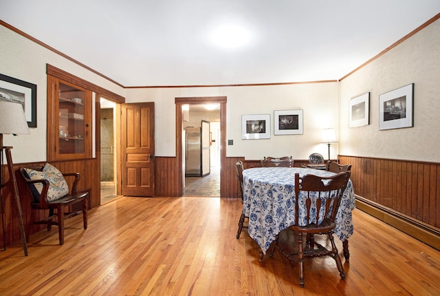 dining space with wainscoting, light wood-style floors, crown molding, wood walls, and a baseboard radiator
