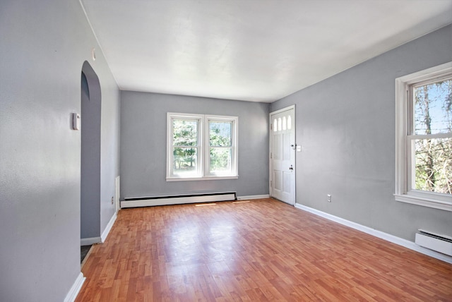 unfurnished living room featuring a baseboard radiator, arched walkways, light wood-style flooring, and baseboards