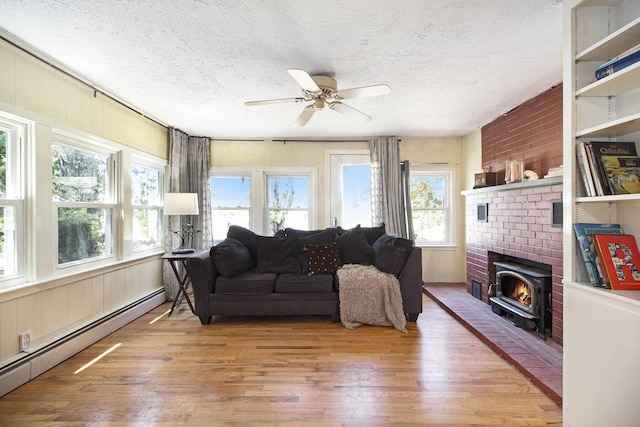 living room with a baseboard heating unit, a wood stove, light wood-style floors, a textured ceiling, and healthy amount of natural light