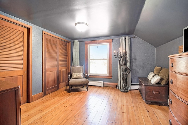 living area featuring baseboard heating, hardwood / wood-style floors, vaulted ceiling, and baseboards