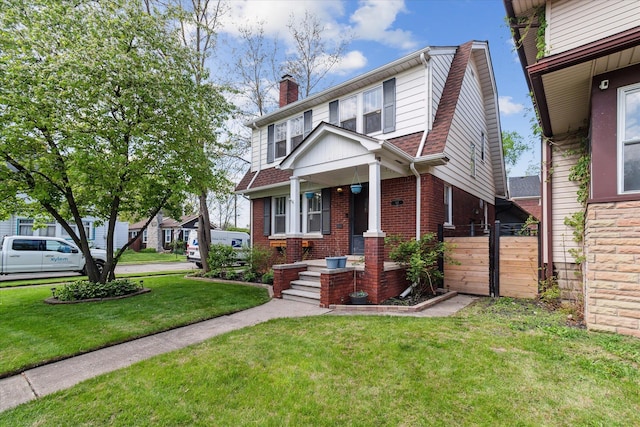 view of front facade with a chimney, a porch, brick siding, and a front lawn