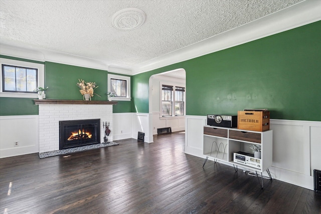 living room with a wainscoted wall, wood finished floors, a textured ceiling, a brick fireplace, and arched walkways