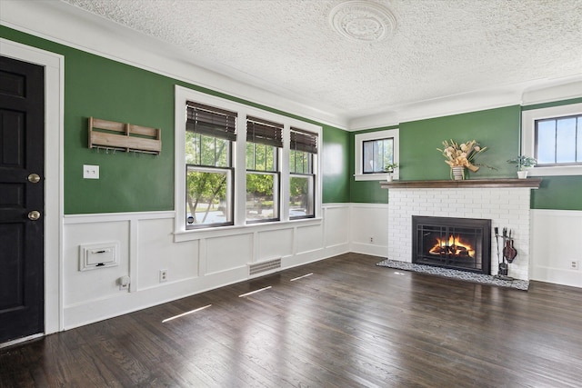 unfurnished living room featuring a fireplace, a textured ceiling, a wainscoted wall, and visible vents