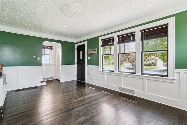 interior space with a wainscoted wall, a textured ceiling, visible vents, and arched walkways
