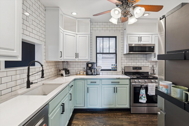 kitchen featuring a sink, stainless steel appliances, ceiling fan, dark wood-style flooring, and backsplash