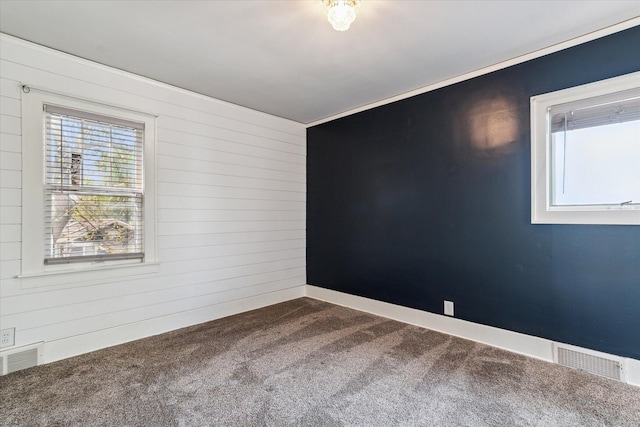 empty room featuring carpet flooring, wooden walls, and visible vents