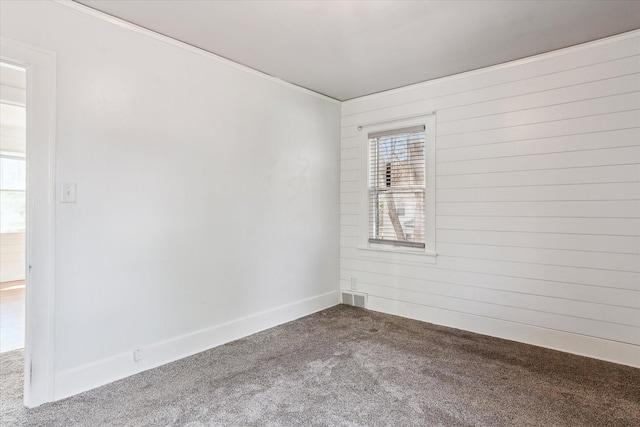 carpeted spare room featuring crown molding, wooden walls, and baseboards