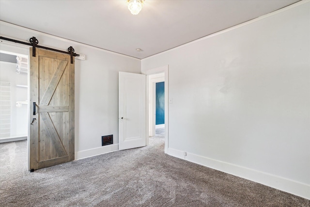 carpeted spare room with ornamental molding, a barn door, baseboards, and visible vents