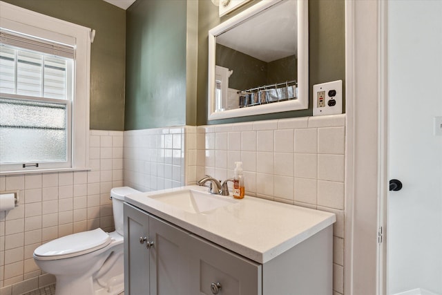 full bathroom with toilet, tile walls, vanity, and a wainscoted wall