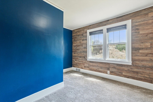 carpeted empty room with wood walls, baseboards, and visible vents
