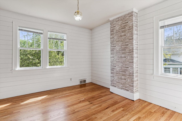 unfurnished room featuring crown molding, wooden walls, light wood finished floors, and visible vents