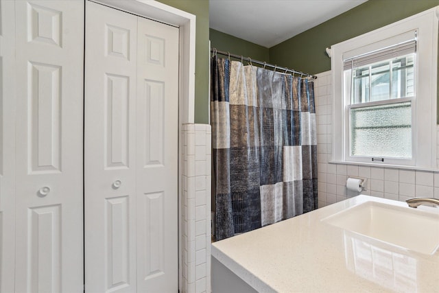 full bathroom with a closet, tile walls, a shower with curtain, and a sink