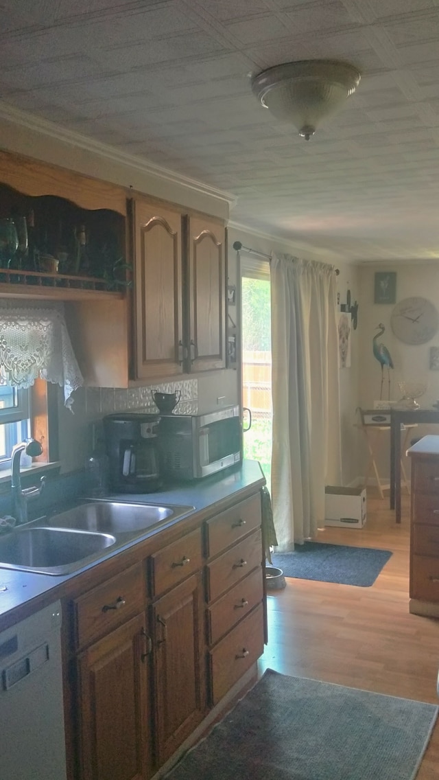 kitchen featuring dishwashing machine, a sink, light wood-type flooring, and backsplash