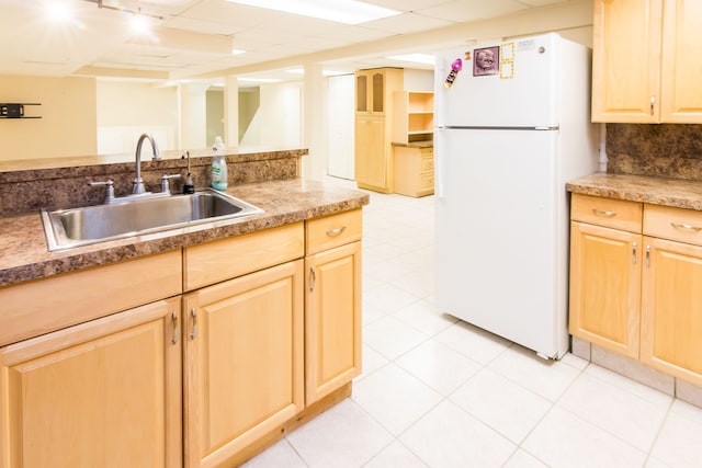 kitchen with freestanding refrigerator, backsplash, light brown cabinets, and a sink