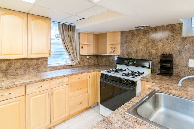 kitchen with light tile patterned floors, a sink, light brown cabinets, range with gas stovetop, and tasteful backsplash