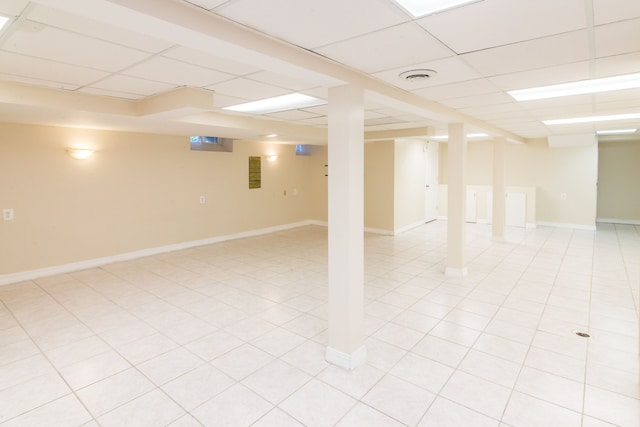 finished below grade area featuring light tile patterned floors, baseboards, and a paneled ceiling